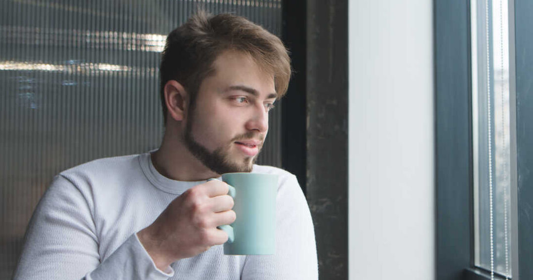 man with coffee in mug sitting next to window