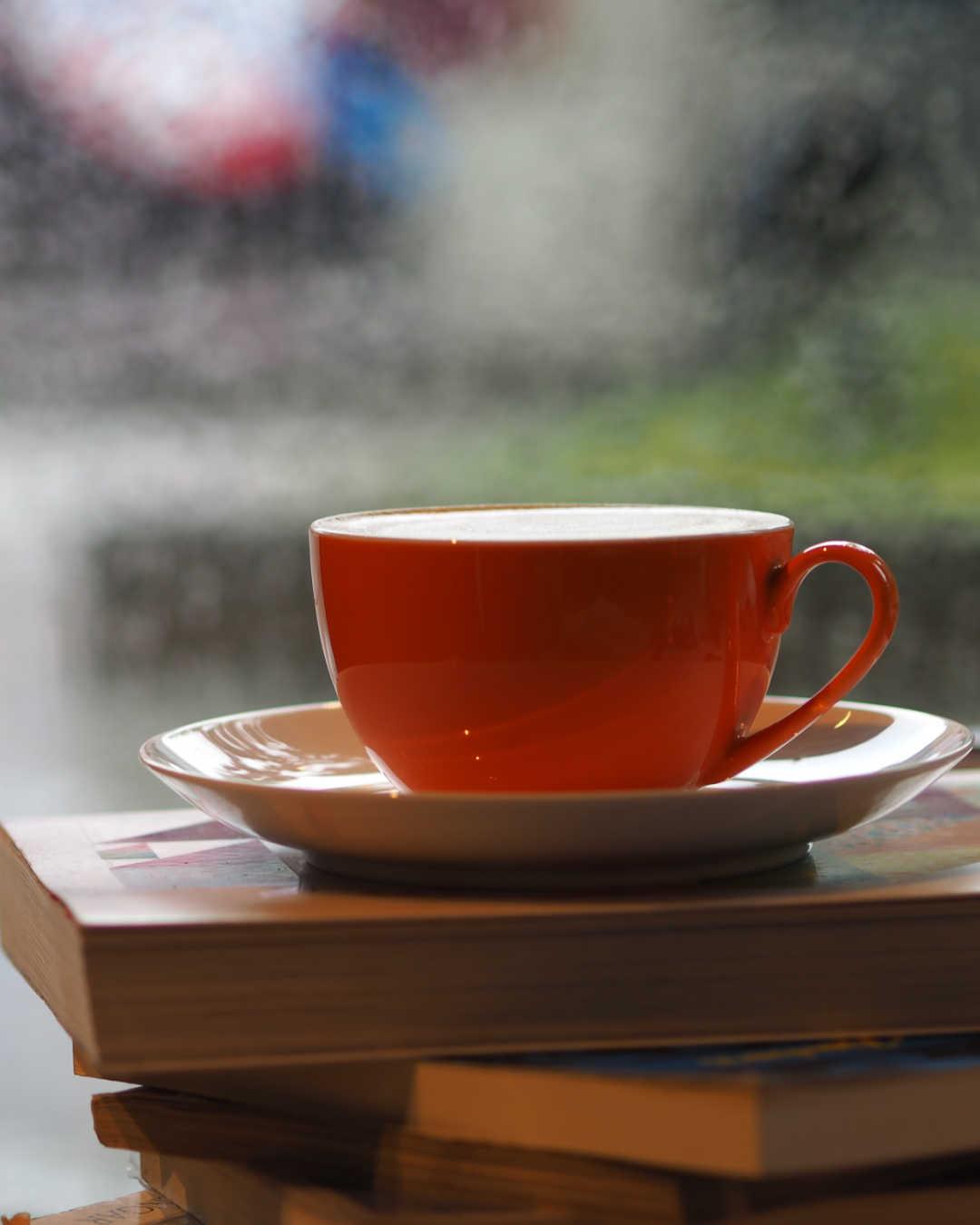 coffee mug on books in front of window, raining outsude